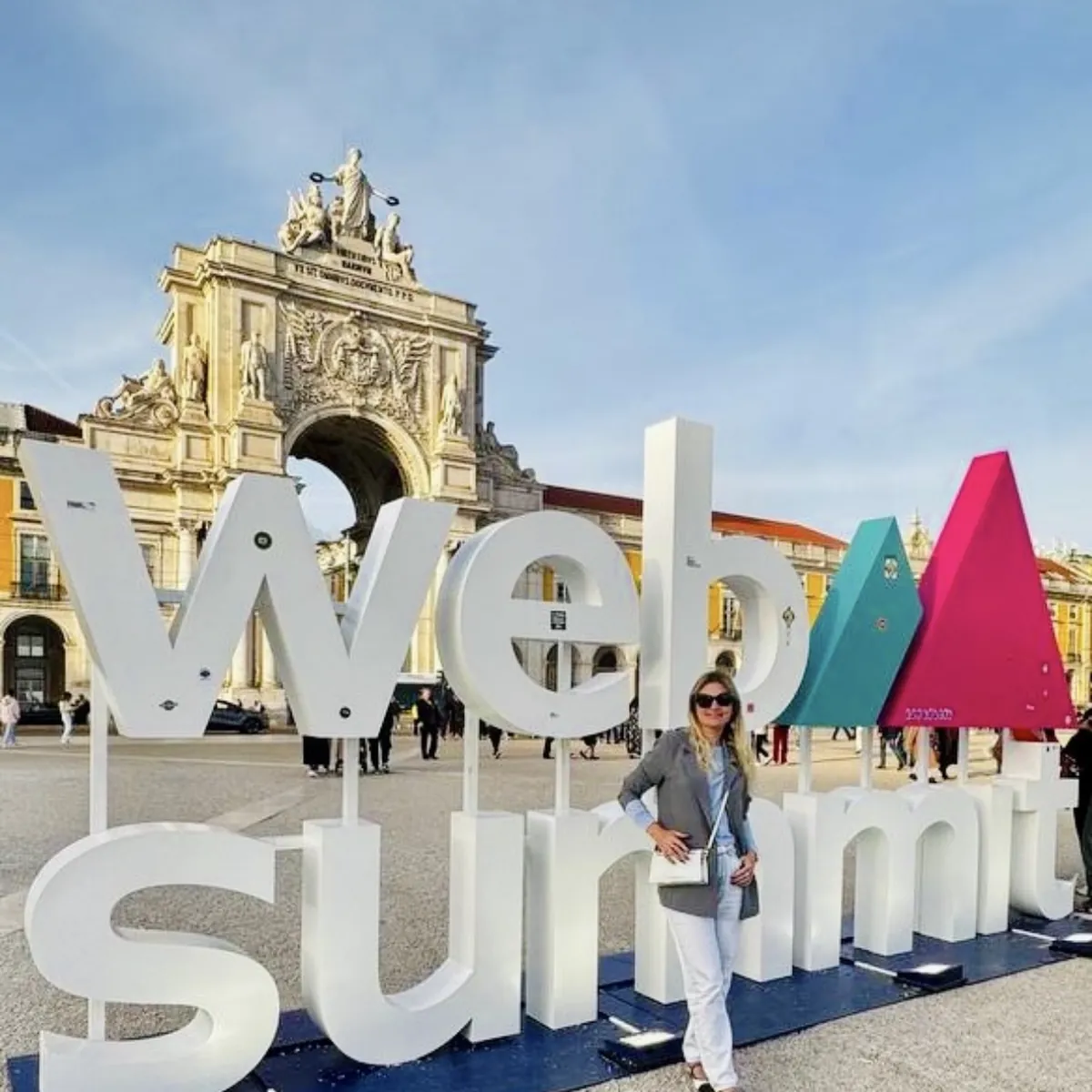 A woman standing beside the Web Summit sign in front of the Rua Augusta Arch in Lisbon